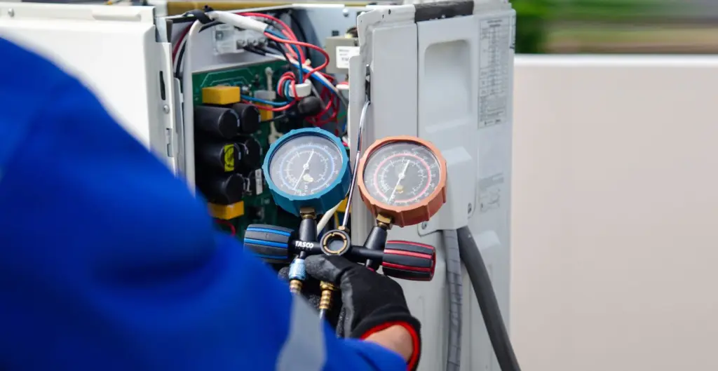 Gloved technician holds manifold gauges connected to an open outdoor air conditioning unit during a refrigerant check.