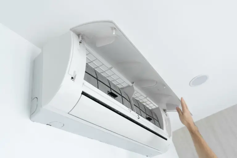 Hand opening the front cover of a wall-mounted ductless mini split unit, exposing the air filters inside.