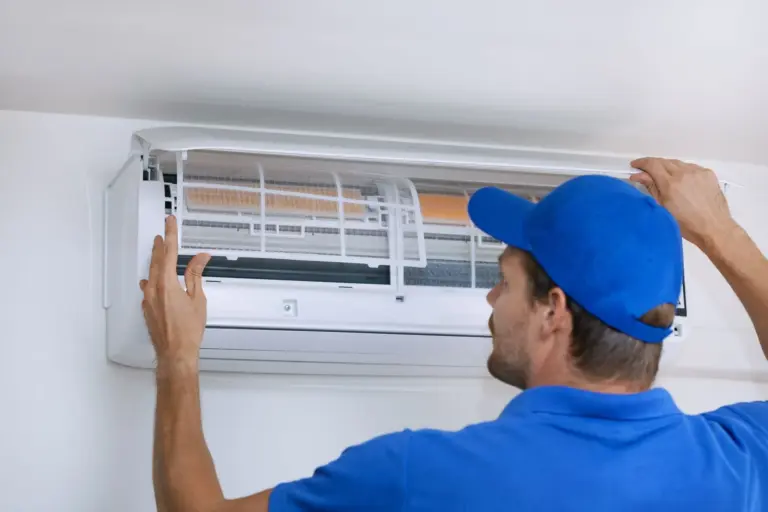 Technician in a blue cap and shirt lifts the front panel of a wall-mounted ductless mini split to access the air filters.